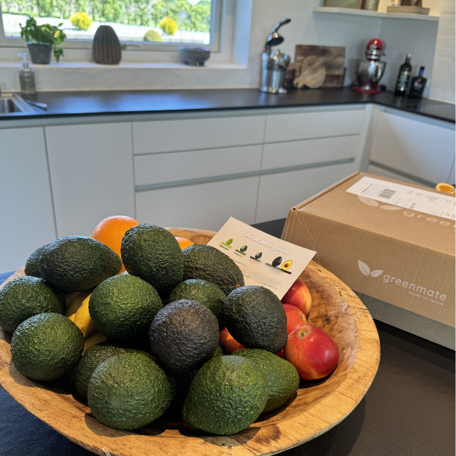 Wooden bowl with avocados and apples on a kitchen counter with a Greenmate box in the background.