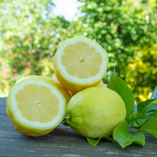 Three lemons, one sliced open, on a wooden surface with a blurred green outdoor background.