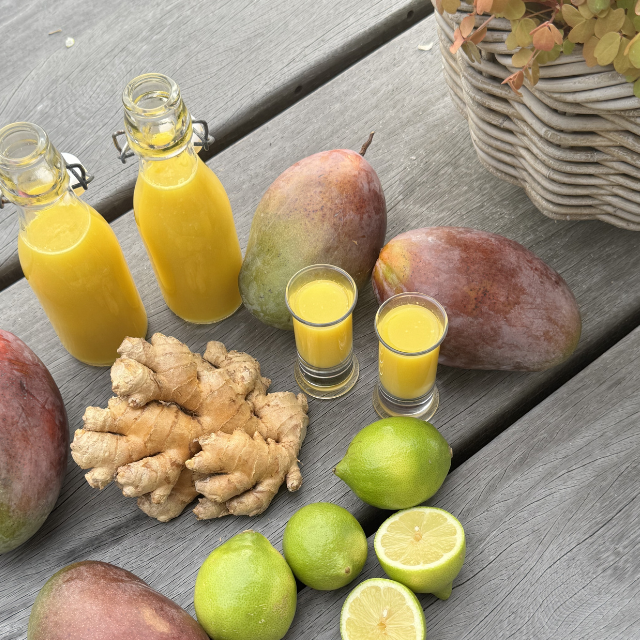 Mango juice in bottles and glasses with mangoes, ginger, and limes on a wooden surface.