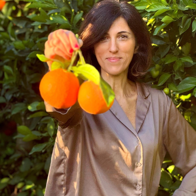Woman with two organic oranges on one hand on an orange farm