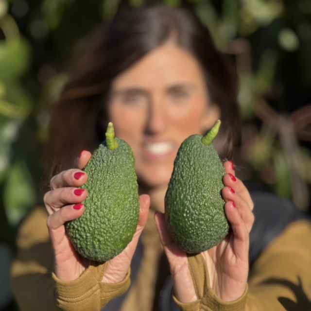 Woman holding two green avocados with a blurred natural background