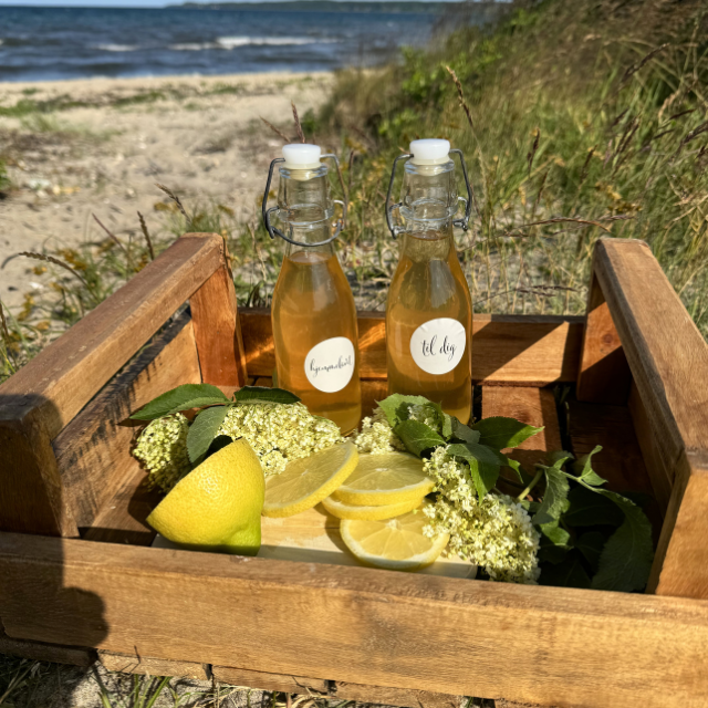 Two bottles of lemonade with lemon slices and flowers in a wooden crate on a beach.